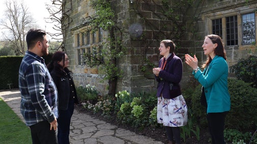 Four people standing outside a stone building, engaged in conversation. One of them is demonstrating British Sign Language.